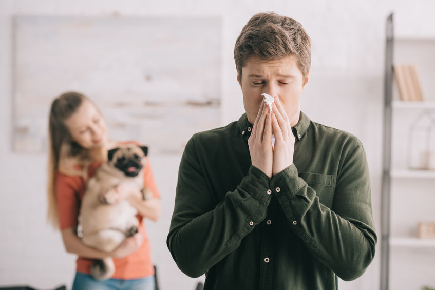 Selective focus of man sneezing in tissue with closed eyes while standing near woman with dog