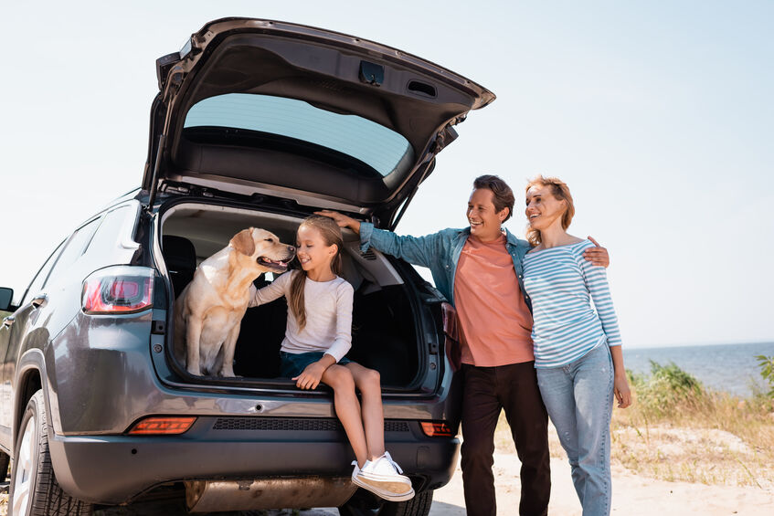 Man hugging wife near daughter and golden retriever in car truck on beach